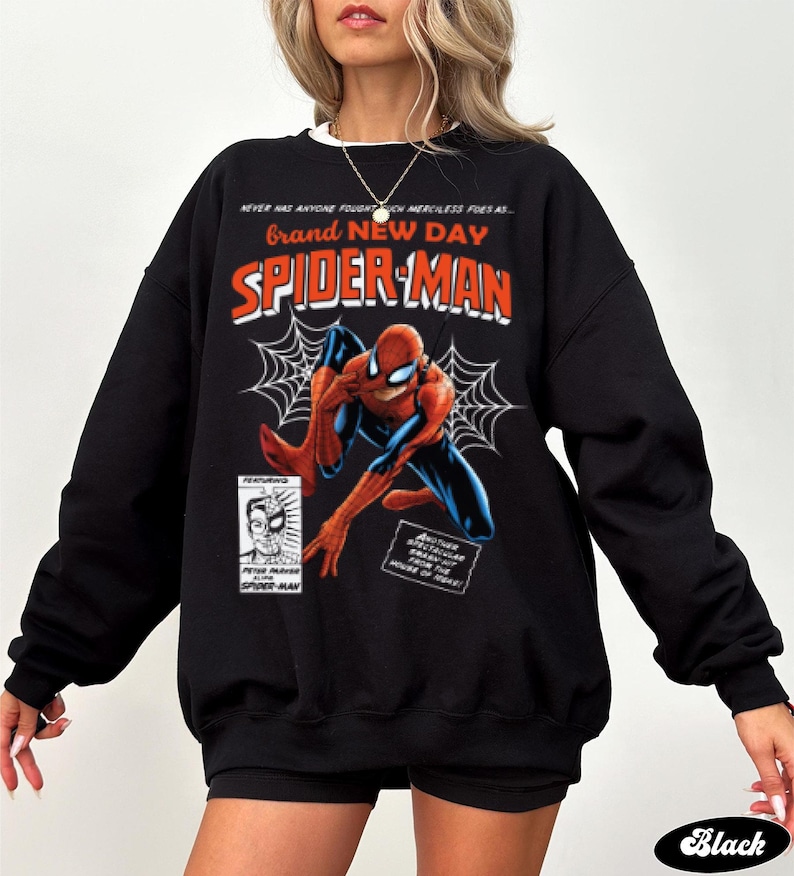 K&ouml;nnte beinhalten: Schwarzes Sweatshirt mit einem Spider-Man-Comic-Design. Die Grafik zeigt die Worte "Brand New Day" und "Spider-Man" in Rot und Orange, zusammen mit einer Illustration von Spider-Man. Das Sweatshirt hat einen wei&szlig;en Kragen.