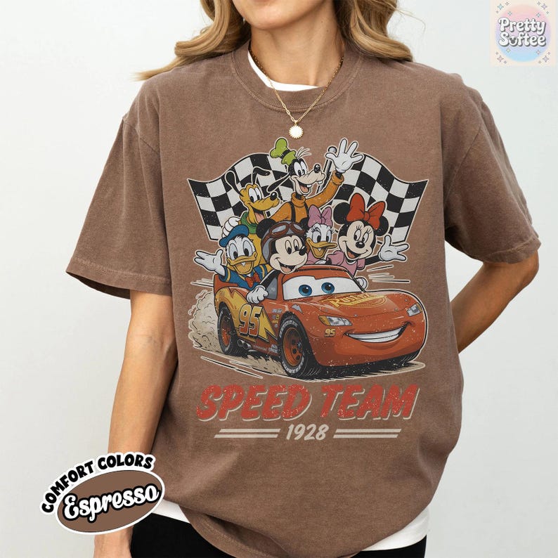 K&ouml;nnte beinhalten: Braunes T-Shirt mit einem Disney-Motiv, das Micky Maus, Donald Duck und Lightning McQueen in einem Rennwagen zeigt. Der Text "SPEED TEAM 1928" ist darunter aufgedruckt. Das Shirt hat einen Vintage-Look und ist im Comfort Colors-Stil gehalten.