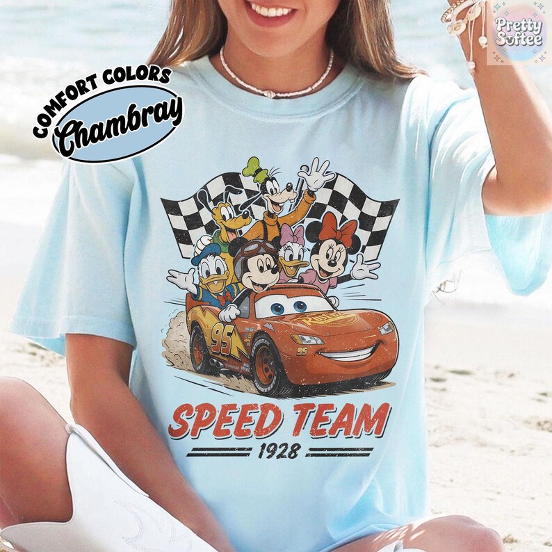 K&ouml;nnte beinhalten: Hellblaues T-Shirt mit einer Grafik von Disney-Figuren in einem Rennwagen. Das Design umfasst Micky Maus, Donald Duck, Goofy sowie Minnie und Daisy Duck. Die Worte "SPEED TEAM 1928" sind darunter gedruckt.