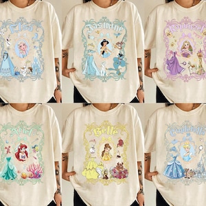 Pu&ograve; includere: T-shirt color crema con disegni di principesse. Ogni maglietta presenta una principessa diversa: Elsa, Jasmine, Rapunzel, Ariel, Belle e Cenerentola. I disegni includono il nome della principessa e immagini correlate.