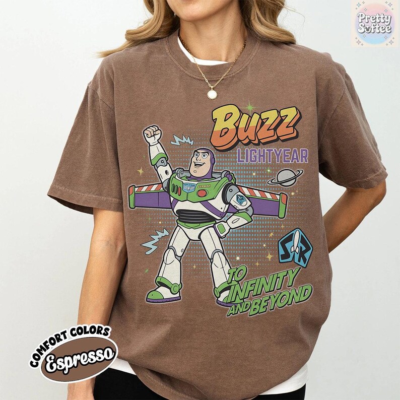 May include: Espresso-coloured t-shirt with a Buzz Lightyear graphic from Toy Story. The design includes the text "Buzz Lightyear" and "To Infinity and Beyond." The shirt has a crew neck and short sleeves.