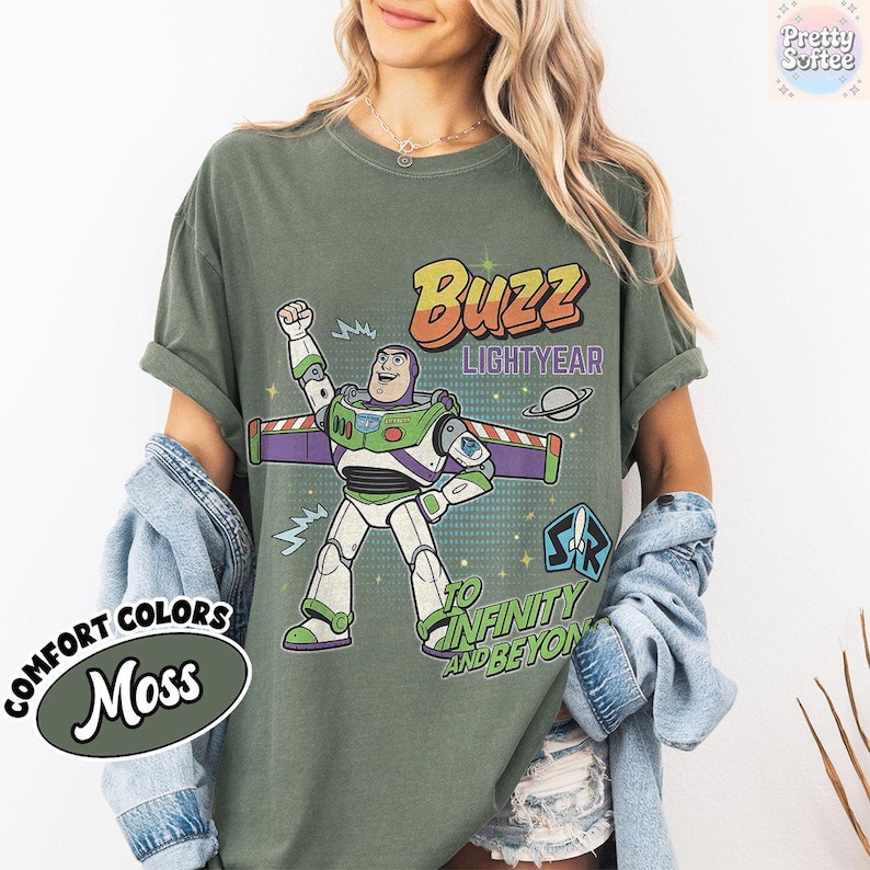 May include: Moss green t-shirt with a Buzz Lightyear graphic and the phrases "Buzz Lightyear" and "To Infinity and Beyond." The shirt also features the words "Comfort Colors" and "Moss" in a circular design.