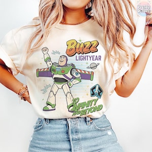 May include: A cream-coloured t-shirt with a graphic of Buzz Lightyear from Toy Story. The design includes the text "Buzz Lightyear" and "To Infinity and Beyond" with a rocket ship and planet. The character is in a dynamic pose.