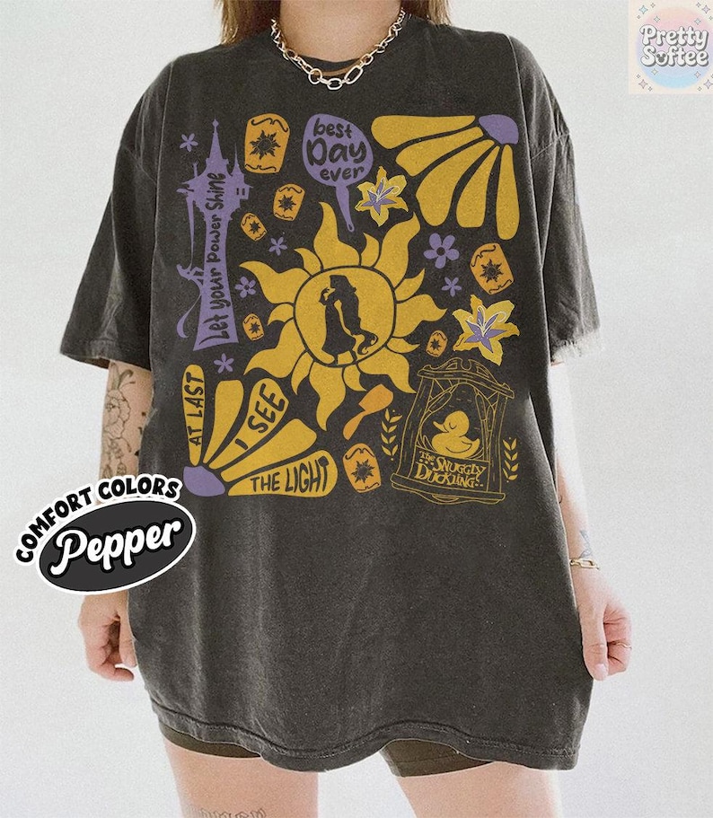 K&ouml;nnte beinhalten: Dunkelgraues &uuml;bergro&szlig;es T-Shirt mit einem Grafikdesign mit Sonne, Blumen und Text. Der Text enth&auml;lt "Best Day Ever", "I See The Light" und "The Snuggly Duckling". Das Shirt hat auch die W&ouml;rter "Comfort Colors" und "Pepper".