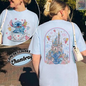 May include: Light blue t-shirt with a graphic of Stitch and a castle. The front features Stitch in a teacup with hearts and balloons. The back has a castle design with Stitch and fireworks. The shirt is labeled "Comfort Colors Chambray".