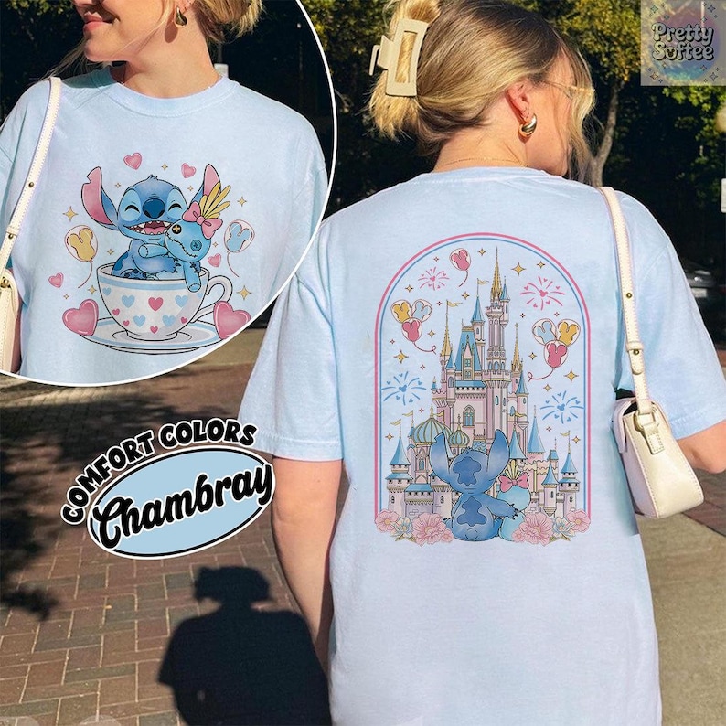 May include: Light blue t-shirt with a graphic of Stitch and a castle. The front features Stitch in a teacup with hearts and balloons. The back has a castle design with Stitch and fireworks. The shirt is labeled "Comfort Colors Chambray".