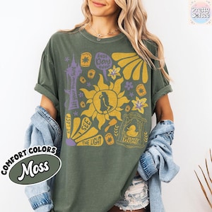 K&ouml;nnte beinhalten: Moosgr&uuml;nes T-Shirt mit einem grafischen Design mit einer Sonne, einer Personensilhouette und dem Text &bdquo;Best Day Ever&ldquo; und &bdquo;I See The Light&ldquo;. Das Shirt tr&auml;gt auch die Aufschrift &bdquo;Comfort Colors&ldquo; und &bdquo;Moss&ldquo;.