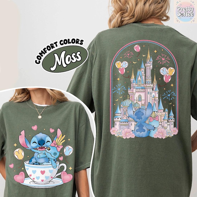 May include: Moss green t-shirt featuring a cartoon illustration of Stitch and Angel. The front shows Stitch and Angel in a teacup with hearts. The back displays a castle with fireworks and balloons. The text "COMFORT COLORS" and "Moss" are also visible.