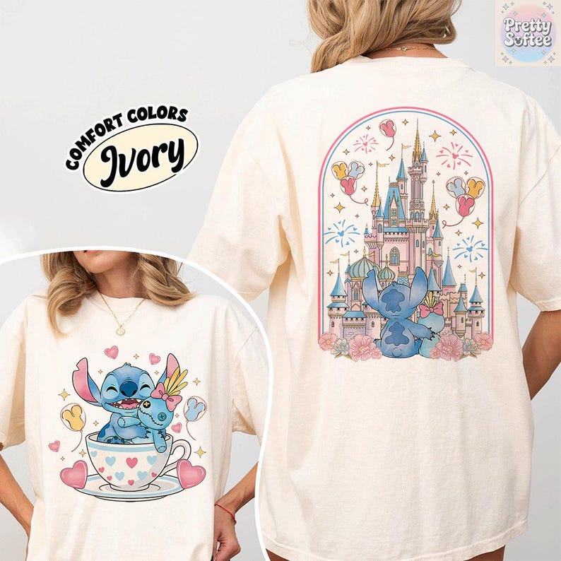 May include: Ivory-colored t-shirt featuring a cartoon illustration of Stitch and Angel in a teacup, with hearts and balloons. The back of the shirt displays a castle scene with Stitch and Angel. The text "COMFORT COLORS" and "Ivory" are also visible.