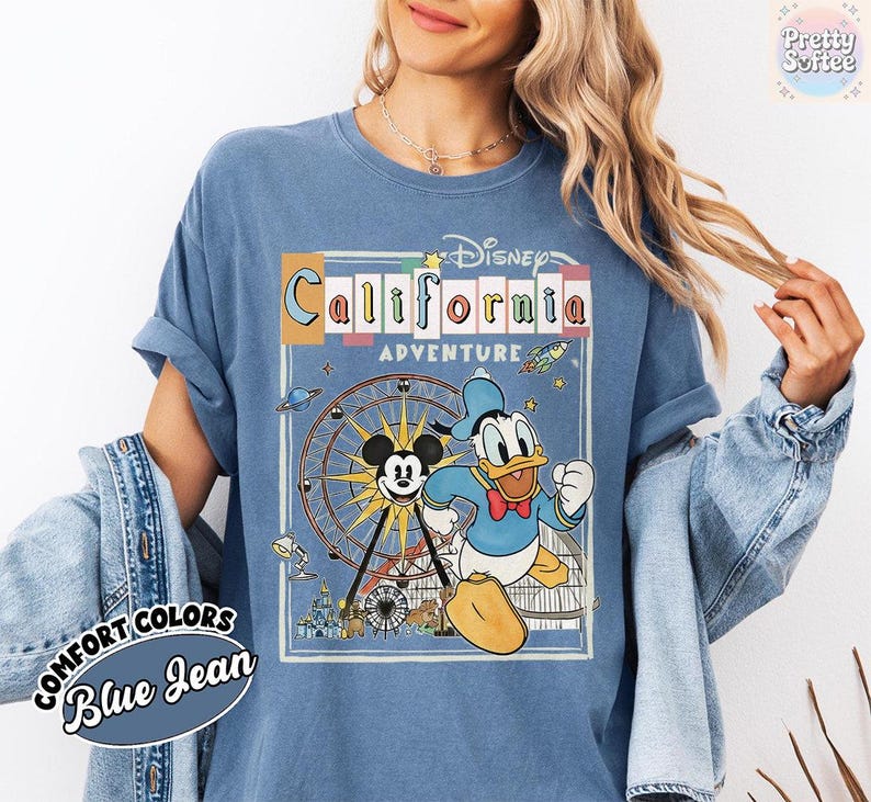 Puede incluir: Camiseta azul Comfort Colors con un dise&ntilde;o de Disney California Adventure. El dise&ntilde;o incluye a Mickey Mouse, el Pato Donald, una noria y el texto "California Adventure". Las mangas est&aacute;n dobladas.