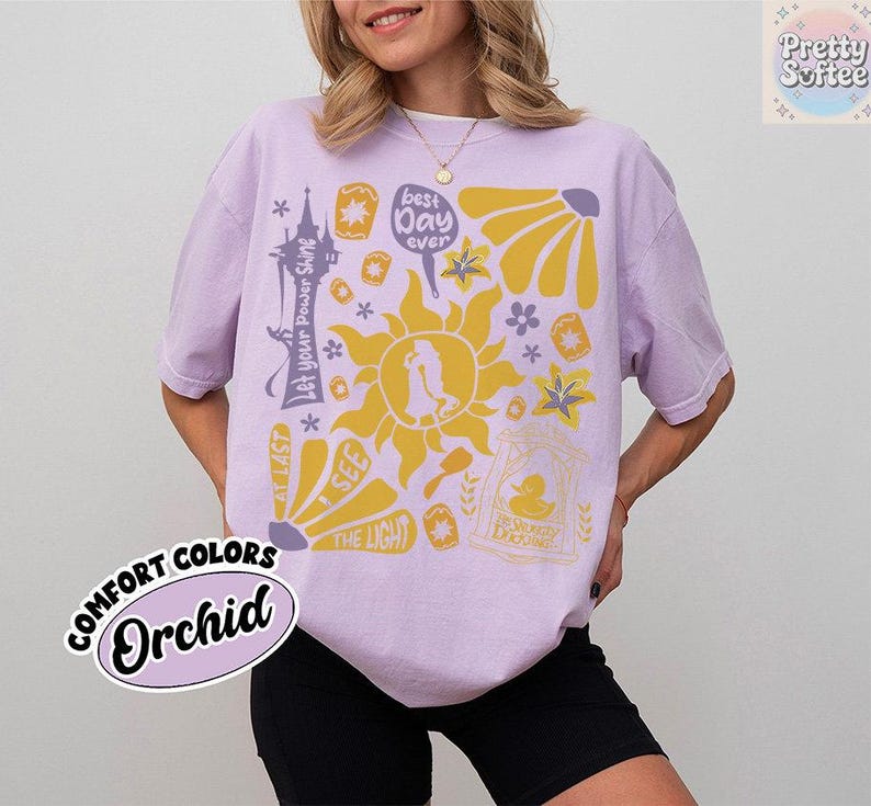 K&ouml;nnte beinhalten: Ein helllila T-Shirt mit einem gelben Grafikdesign mit einer Sonne, Blumen und Text. Der Text enth&auml;lt "best day ever", "Let your Power Shine" und "At Last I See the Light". Das Shirt ist mit "Comfort Colors Orchid" gekennzeichnet.
