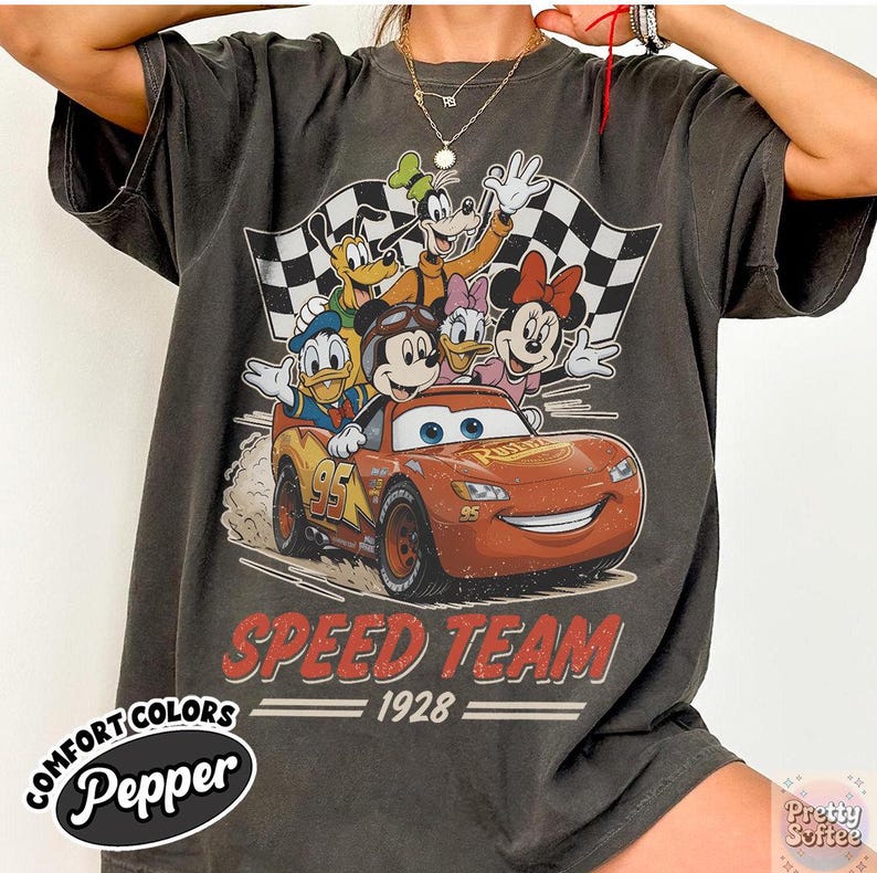K&ouml;nnte beinhalten: Dunkelgraues T-Shirt mit einer Grafik von Disney-Figuren, darunter Micky Maus und Donald Duck, mit einem roten Rennwagen. Der Text "SPEED TEAM 1928" ist unter dem Bild aufgedruckt. Das Shirt hat die Worte "Comfort Colors Pepper" aufgedruckt.