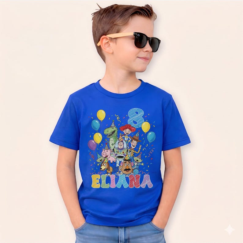May include: A royal blue t-shirt featuring a colorful graphic of Toy Story characters, balloons, confetti, the number 8, and the name "ELIANA" in rainbow letters. The child is wearing sunglasses.