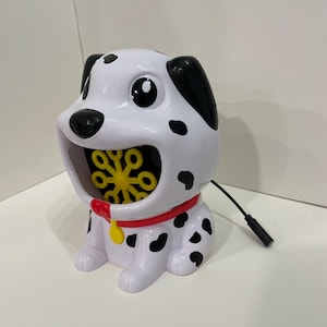 May include: A white and black Dalmatian dog-shaped bubble blower with a red collar and yellow buckle. The blower has a yellow and black bubble wand inside its mouth.