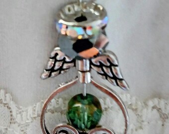 May include: A handcrafted angel pendant with a silver-tone metal frame. The pendant features a green faceted bead, a brown faceted bead, and iridescent wings. The angel's head is a small, silver-tone can lid. The pendant hangs from a delicate chain.
