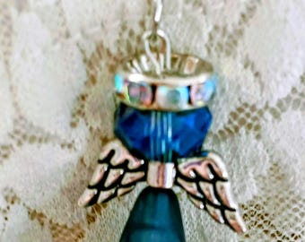 May include: A silver-toned necklace featuring a pendant in the shape of an angel. The angel has blue and silver wings, a blue body, and a dark blue skirt. A pearl-like bead hangs at the bottom.