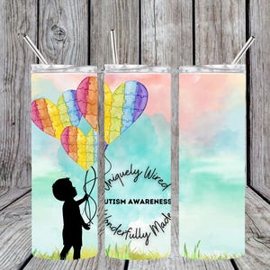 Puede incluir: Un vaso de acero inoxidable con un fondo de acuarela y una silueta de un niño sosteniendo globos en forma de corazón de rompecabezas de arcoíris. El vaso tiene el texto "Uniquely Wired Autism Awareness Wonderfully Made".