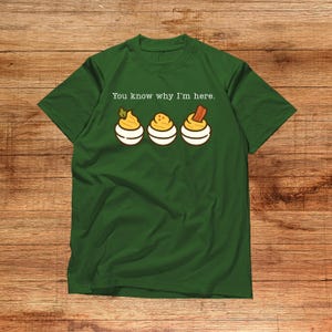 May include: Green t-shirt with the text "You know why I'm here." The shirt features a graphic of three deviled eggs, each with a different topping. The shirt is made of a soft material.