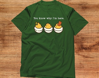 May include: Green t-shirt with the text "You know why I'm here." The shirt features a graphic of three deviled eggs, each with a different topping. The shirt is made of a soft material.