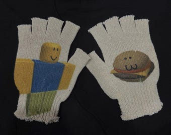 May include: A pair of fingerless gloves with a beige background. One glove features a printed image of a Roblox character, while the other glove features a printed image of a hamburger with a smiley face.