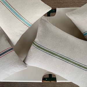 May include: Four decorative throw pillows with different colored stripes. The pillows are made of a natural linen fabric and have a rustic, farmhouse style.