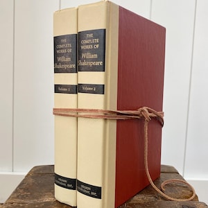 May include: A white ceramic mug with a black handle and the text "But First, Coffee" in a bold, black font. The mug is set against a blurred background, suggesting a cozy setting. The mug appears to be approximately 4 inches tall.