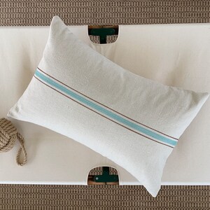 May include: A white pillow with a blue and brown stripe on a white canvas cot.