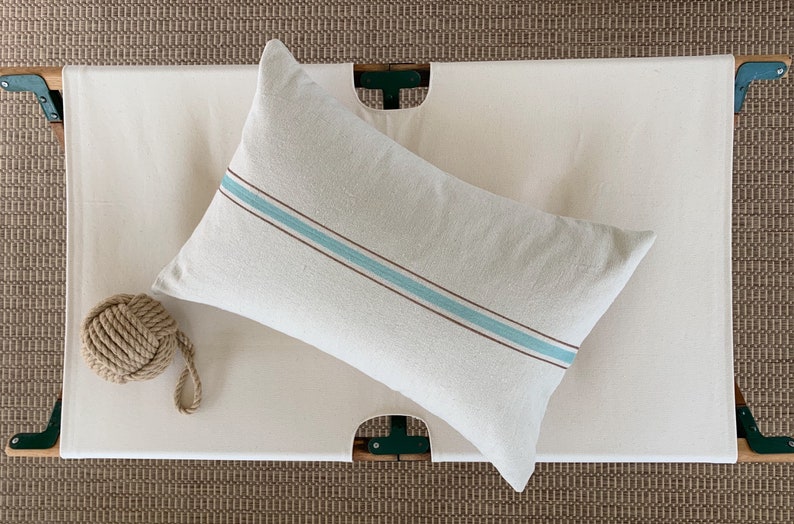 May include: A white pillow with a blue and brown stripe on a white canvas cot.