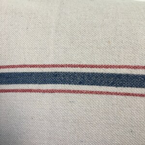 May include: A white fabric pillow with two red stripes and one blue stripe.