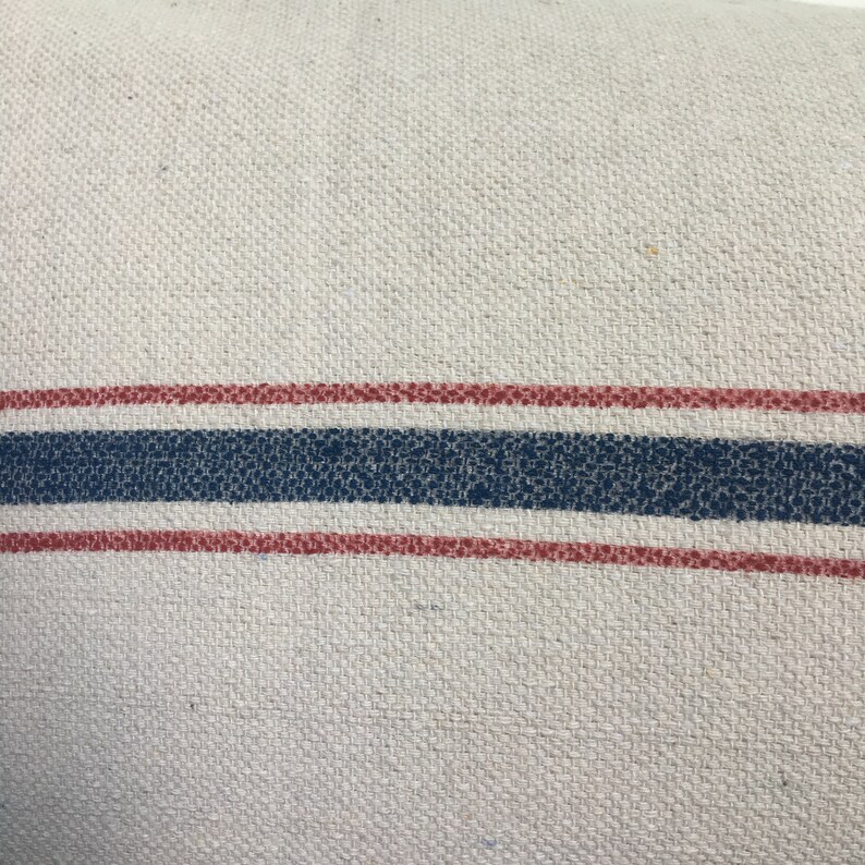 May include: A white fabric pillow with two red stripes and one blue stripe.