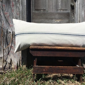 May include: A long, white lumbar pillow with two blue stripes. The pillow is sitting on a wooden stool.