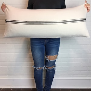 May include: A white rectangular pillow with two black stripes across the center. The pillow is being held by a person.