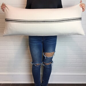 May include: A white rectangular pillow with two black stripes across the center. The pillow is being held by a person.