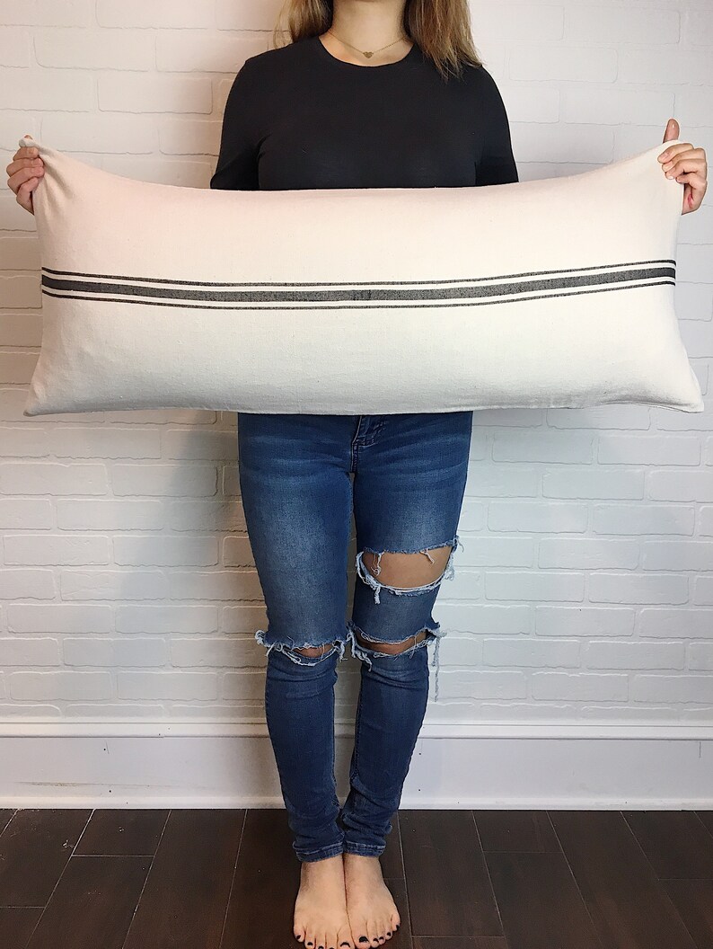 May include: A white rectangular pillow with two black stripes across the center. The pillow is being held by a person.