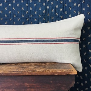 May include: A white linen pillow with red and blue stripes. The pillow is sitting on a wooden surface.