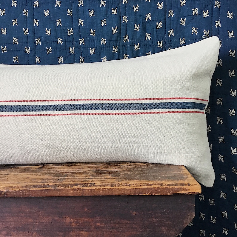 May include: A white linen pillow with red and blue stripes. The pillow is sitting on a wooden surface.