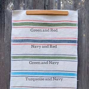 May include: A white fabric sample with five different colored stripes. The stripes are labeled with the colors: Green and Red, Navy and Red, Green and Navy, Turquoise and Navy, and Ocean Blue and Brown.