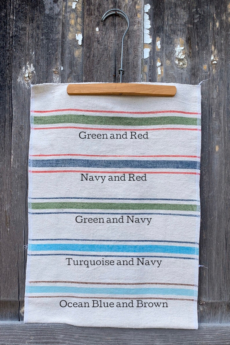 May include: A white fabric sample with five different colored stripes. The stripes are labeled with the colors: Green and Red, Navy and Red, Green and Navy, Turquoise and Navy, and Ocean Blue and Brown.