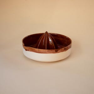 May include: A ceramic citrus juicer with a white base and a brown rim and juicing cone. The juicer is designed with a spout for easy pouring. The cone is a dark brown color.