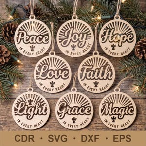 May include: Eight circular light-colored wooden ornaments featuring laser-cut designs. Each ornament displays a unique word: Peace, Joy, Hope, Love, Faith, Light, Grace, or Magic, accompanied by a small angel icon and the text IN EVERY HEART.