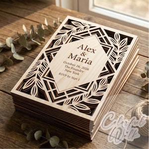 Op de afbeelding: Een stapel lasergesneden houten huwelijksuitnodigingen. De bovenste uitnodiging bevat de namen "Alex & Maria" en evenementdetails. Het ontwerp omvat geometrische vormen en bladerpatronen. De uitnodigingen liggen op een houten oppervlak.