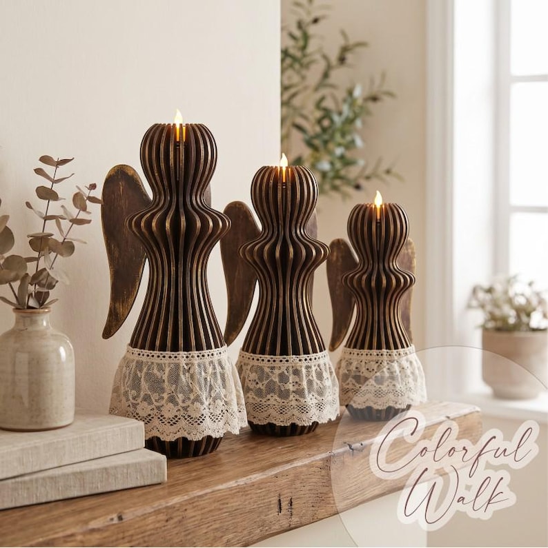 May include: Three dark brown wooden angel-shaped candle holders of varying heights, each featuring vertical slats and a white lace trim at the base. Each angel holds a small, lit, battery-operated candle at the top, creating a warm glow.