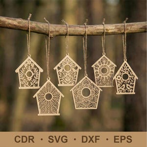 Puede incluir: Seis adornos de madera con forma de casita para pájaros, con intrincados diseños calados, colgados de una rama de árbol. Cada casita presenta un patrón único, incluyendo motivos florales y geométricos. La parte inferior de la imagen muestra el texto: CDR, SVG, DXF, EPS.
