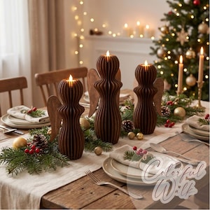 May include: Three dark brown wooden angel-shaped candle holders with vertical slats and glowing tea lights on top. The figures are arranged on a dining table decorated with pine branches, red berries, and gold ornaments for a holiday setting.