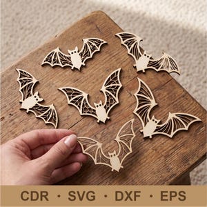 May include: Six laser-cut wooden bat shapes with intricate wing patterns. The bats are light beige in color and feature cut-out details in the wings. The text CDR, SVG, DXF, and EPS is printed at the bottom of the image in a dark brown font.