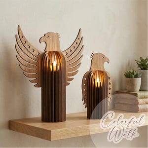 May include: Two wooden eagle candle holders with star cutouts. The eagle heads and wings are light brown, while the bodies are a darker brown. Each holder has a small, glowing candle inside. The candle holders are on a wooden shelf.