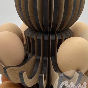 Puede incluir: Un soporte de madera para huevos con un dise&ntilde;o decorativo, que contiene varios huevos marrones. El soporte tiene un dise&ntilde;o en capas, abierto, con secciones marrones oscuras y claras alternas. Los huevos son de color marr&oacute;n natural.