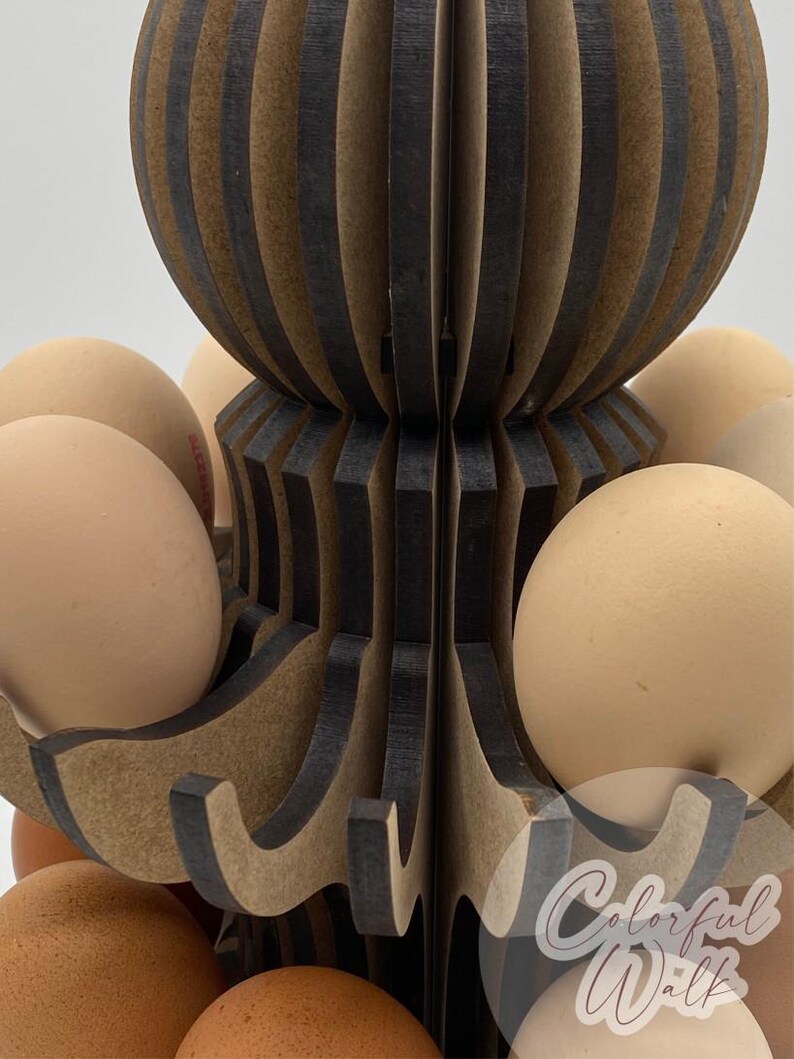 Puede incluir: Un soporte de madera para huevos con un dise&ntilde;o decorativo, que contiene varios huevos marrones. El soporte tiene un dise&ntilde;o en capas, abierto, con secciones marrones oscuras y claras alternas. Los huevos son de color marr&oacute;n natural.