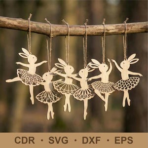 Könnte beinhalten: Sechs Holzornamente in Form von tanzenden Hasen, die an einem Ast hängen. Jedes Ornament ist aus hellem Holz geschnitten und zeigt einen Hasenkopf und einen Tutu mit filigranen Ausschnitten. Aufgehängt mit Schnur.