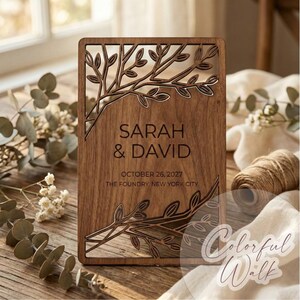 Op de afbeelding: Een rechthoekige houten plaquette met lasergesneden boomtakontwerpen. De plaquette toont de namen "SARAH & DAVID" en de datum "OCTOBER 26, 2027" samen met "THE FOUNDRY, NEW YORK CITY". Het hout heeft een warme, natuurlijke tint.